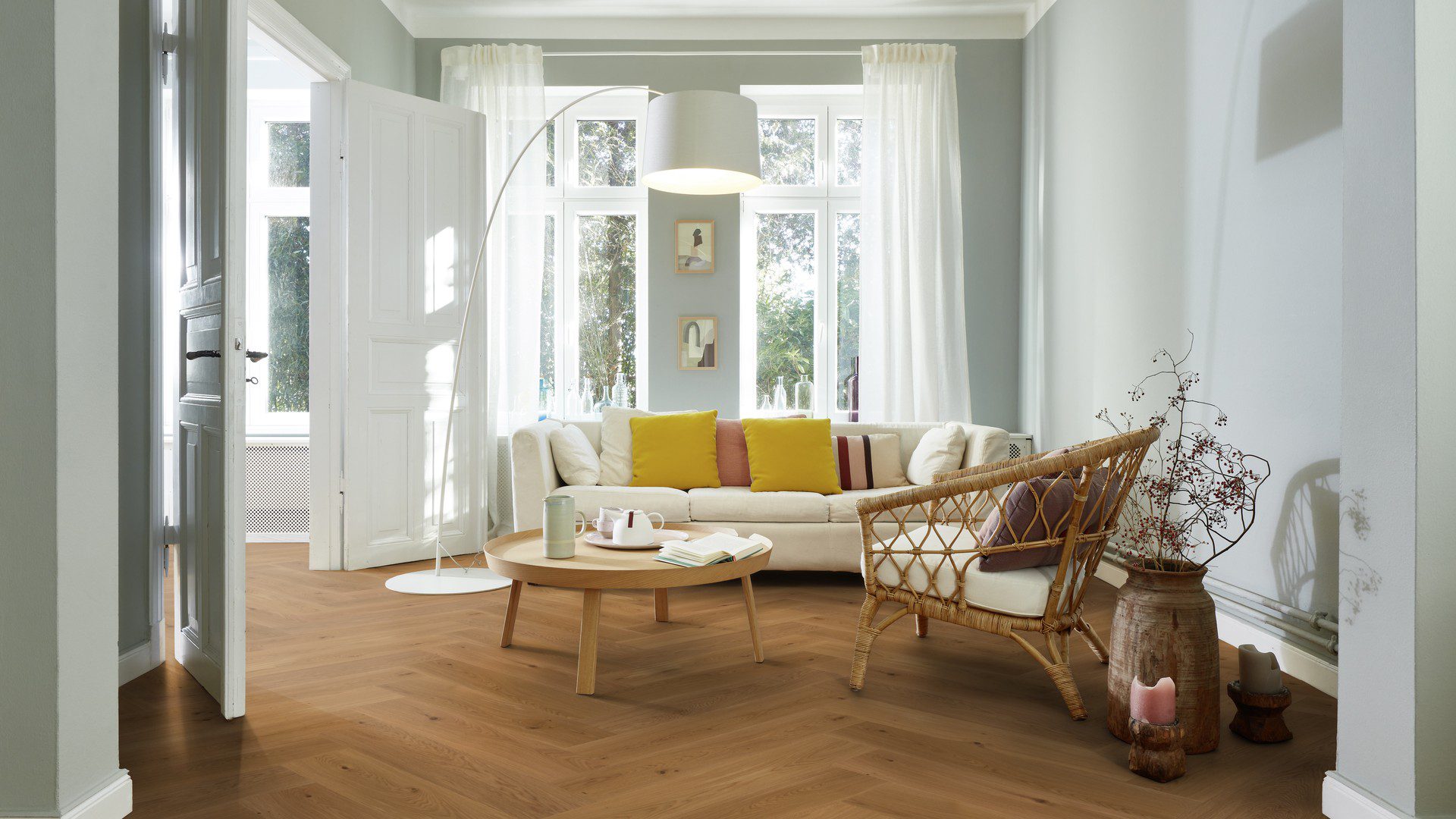 Fischgrätparkett Eiche Mix geölt 180 mm – natürliche Farbnuancen und lebhafte Maserung der Eiche. Verlegt im Wohnzimmer mit weißem Sofa mit gelben Kissen, Couchtisch, Stuhl und Stehlampe.