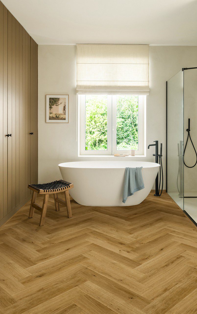 Herringbone laminate floor Quick-Step Impressive Дизайн Cinnamon installed to bathroom floor. White separatly standind bathtub