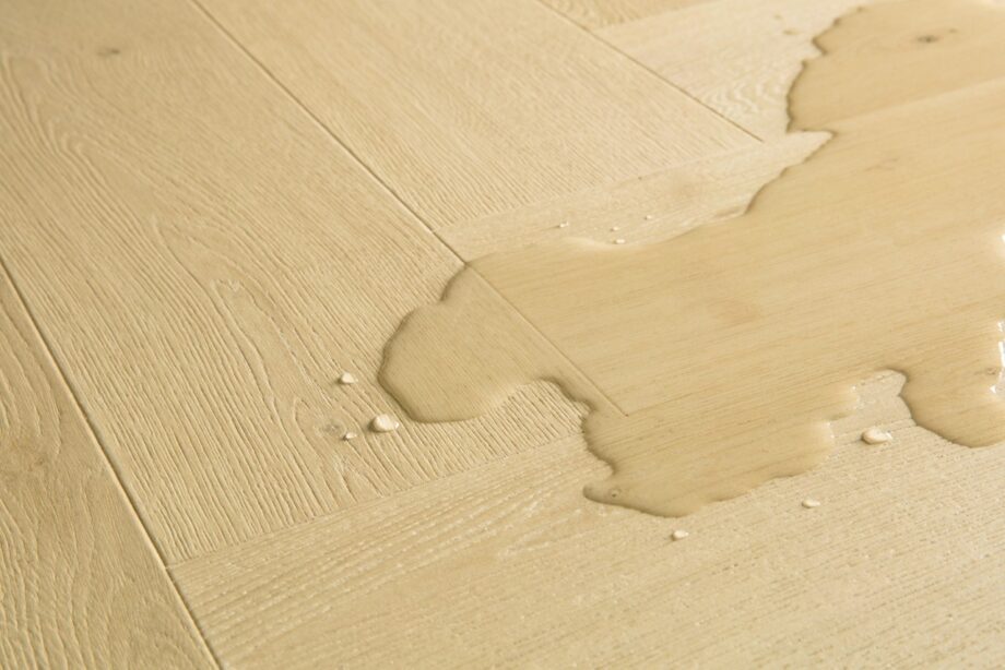 Kalanruoto laminaatti Quick Step Impressive Дизайн Ginger Oak, lämmin keskiruskea tammen sävy ja tasainen lajitelma, vesilätäkkö osoittamassa vedenkestävyyttä