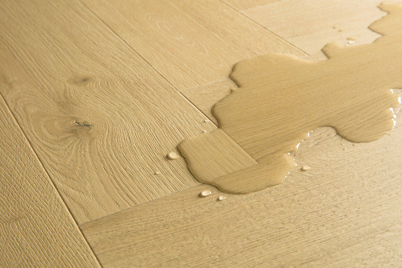 Laminaatti kalanruoto Quick Step Impressive Дизайн Nutmeg Oak, lämmin keskiruskea tammen sävy ja tasainen lajitelma, vesilätäkkö osoittamassa vedenkestävyyttä