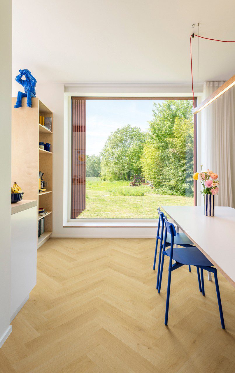 Ламинат ёлочкой Quick Step Impressive Дизайн Nutmeg Oak, уложен на кухонный пол, белый обеденный стол с синими стульями и вазой с цветами