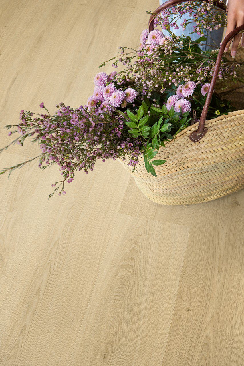 LVT floor Quick-Step Bloom Botanic Beige installed on a floor. On the floor is laying open bag with many different beautiful pink flowers.