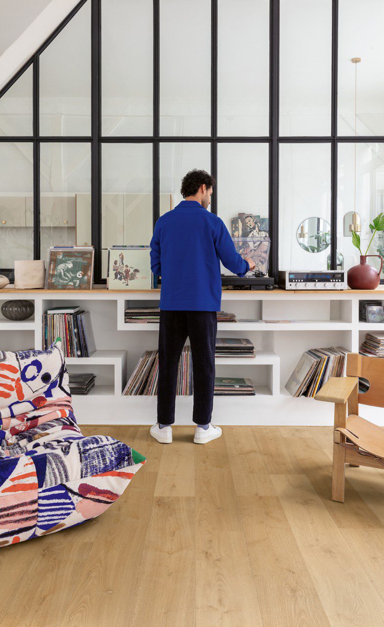 Vinyl flooring Quick-Step Bloom Elegant Oak Natural installed on living room floor. Chairs, shelve, man is busy with vinyl record player.