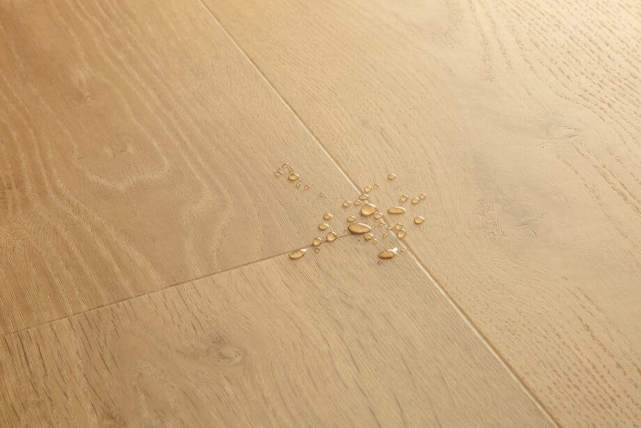 vinyylilattia-quick-step-bloom-elegant-oak-natural Vinyylilattia Quick Step Bloom Elegant Oak Natural, luonnollinen tammen sävy ja lankkudesign, pinnalla vesipisaroita korostamassa lattian vedenkestävyyttä.