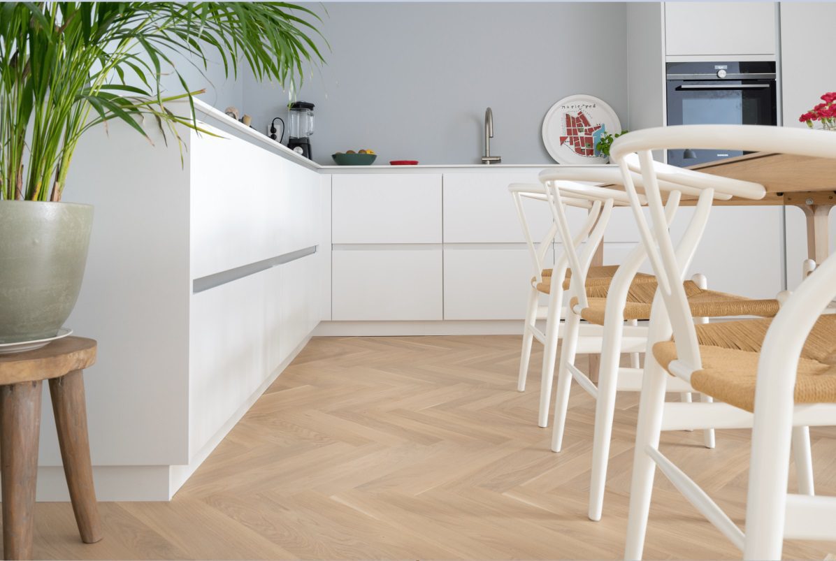 Bauwerk Monopark паркет ёлочка Дуб Crema с покрытием B-Protect уложен на кухонный пол. Кухонная мебель, обеденный стол, стулья.