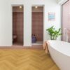 Herringbone laminate floor Quick Step Impressive Дизайн Cumin Oak, installed on bathroom floor with a white bathtub