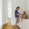 laminat-fischgrat-quick-step-impressive-design-cinnamon-oak Vinylboden Fischgrät Quick Step Impressive Дизайн Cinnamon Oak, verlegt im Badezimmerboden, Vater lässt Wasser aus dem Hahn laufen und das Kind sitzt auf der Badezimmermöbelplatte