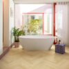 Laminat Fischgrät Quick Step Impressive Дизайн Ginger Oak, verlegt im Badezimmerboden, freistehende weiße Badewanne, mit blauer Mosaikfliese verkleideter Sockel und rote Fensterrahmen