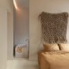 klickvinyl-quick-step-bloom-sea-breeze-oak-light Klickvinyl Quick Step Bloom Sea Breeze Oak Light im Schlafzimmer verlegt, sehr heller Eicheton und Dielendesign, Bett mit schöner hellbrauner Bettwäsche, im Hintergrund ein Badezimmer mit freistehender, eckiger Дизайн-Badewanne.