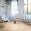Vinyylilankku Quick Step Bloom Pure Oak Blush asennettuna lastenh uoneen lattialle, vaalea tammen sävy kevyellä punertavalla vivahteella ja lankkudesign, kehto, keinul hevonen, tuoli ja leluja.